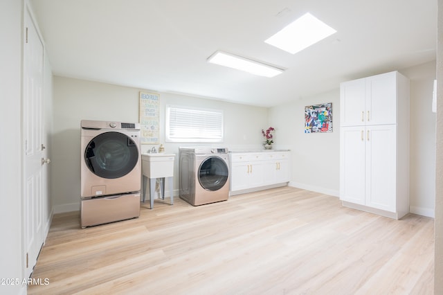 clothes washing area featuring cabinets, a skylight, independent washer and dryer, and light wood-type flooring