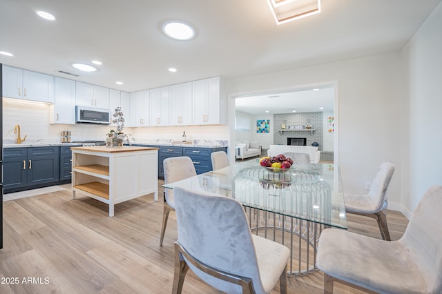 dining room featuring sink, light hardwood / wood-style floors, and a brick fireplace