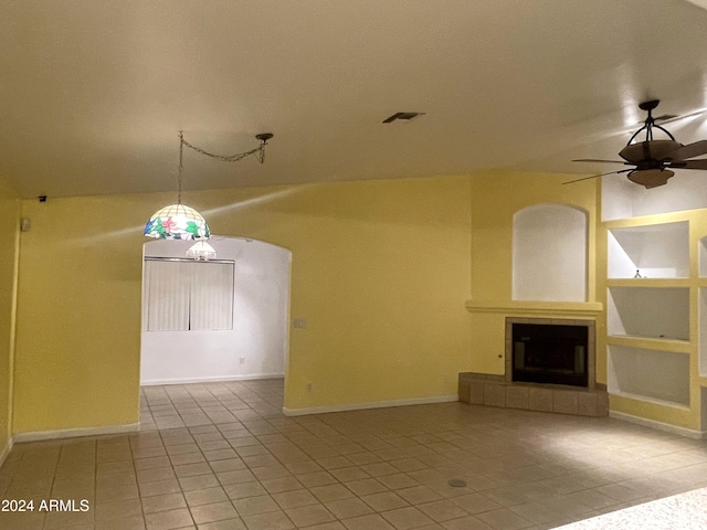 unfurnished living room with a fireplace, built in features, ceiling fan, and light tile patterned flooring