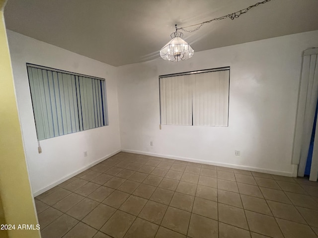 tiled spare room with a chandelier