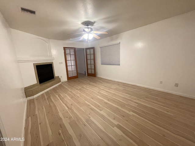 unfurnished living room with a tile fireplace, ceiling fan, french doors, and wood-type flooring