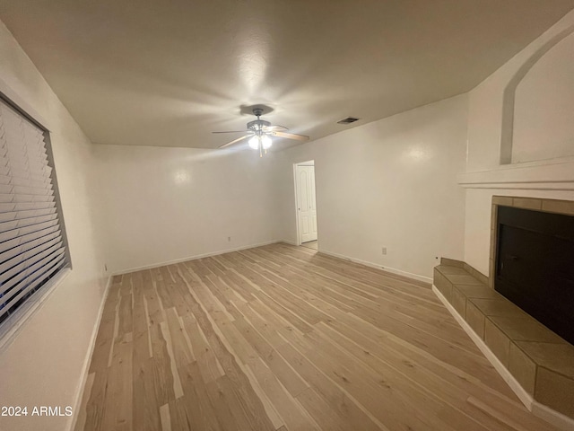 unfurnished living room with a tile fireplace, light hardwood / wood-style floors, and ceiling fan