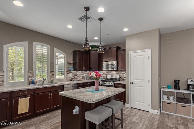 kitchen with tasteful backsplash, visible vents, appliances with stainless steel finishes, a kitchen island, and light wood-type flooring