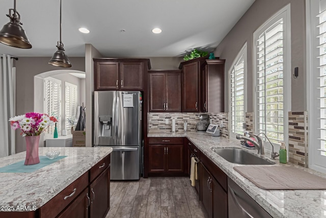 kitchen featuring light stone counters, a sink, light wood-type flooring, stainless steel refrigerator with ice dispenser, and backsplash