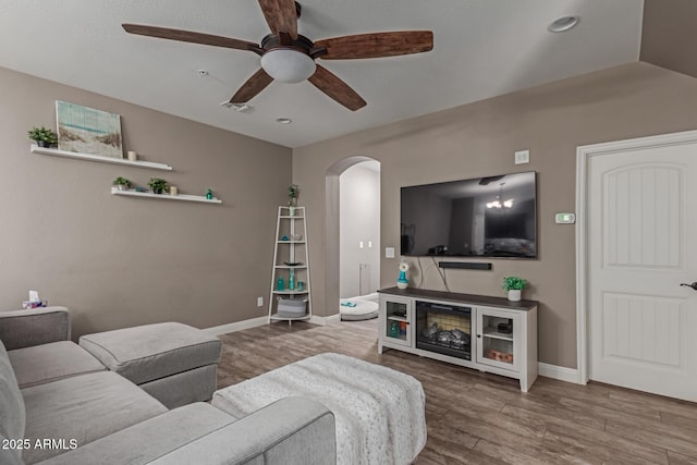 living room with baseboards, arched walkways, a ceiling fan, lofted ceiling, and wood finished floors