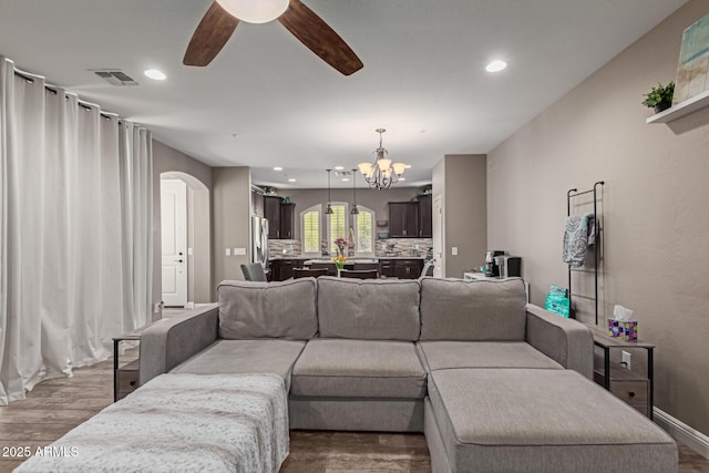 living area featuring arched walkways, recessed lighting, visible vents, wood finished floors, and ceiling fan with notable chandelier