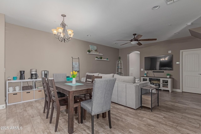 dining space with arched walkways, visible vents, light wood-style floors, baseboards, and ceiling fan with notable chandelier