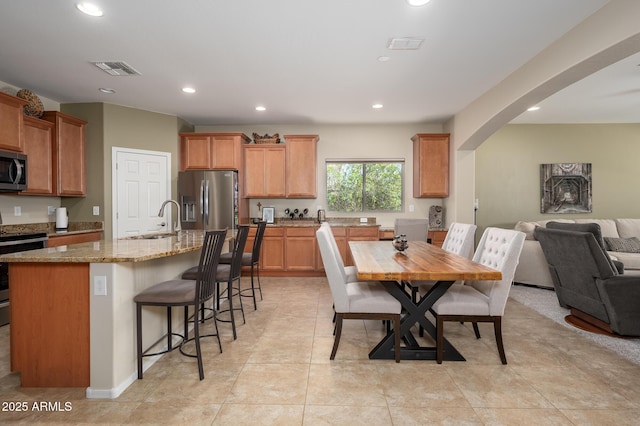 kitchen featuring arched walkways, light stone counters, open floor plan, stainless steel appliances, and a sink