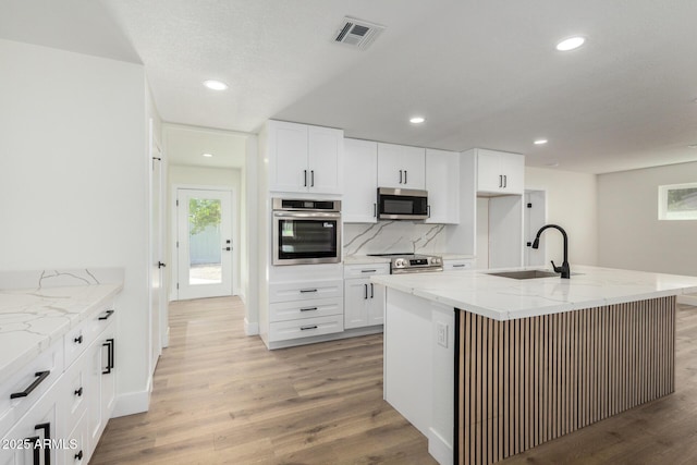 kitchen featuring visible vents, light stone counters, a sink, light wood-style flooring, and appliances with stainless steel finishes