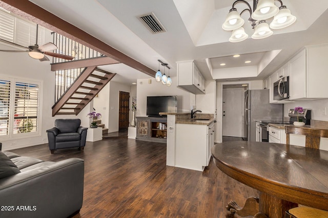 interior space with a raised ceiling, stainless steel appliances, hanging light fixtures, dark stone counters, and white cabinetry