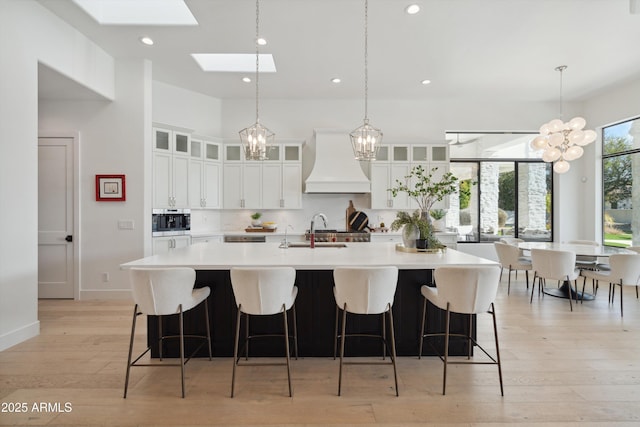 kitchen featuring sink, premium range hood, white cabinetry, an island with sink, and decorative backsplash