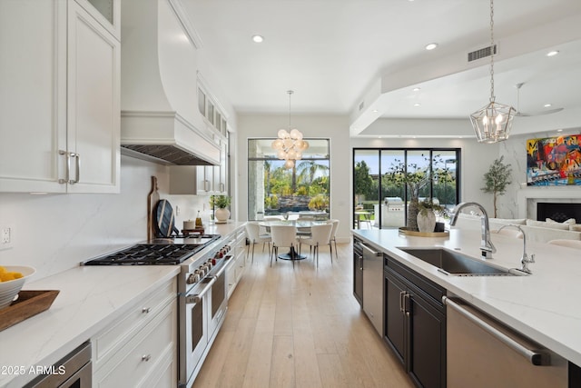 kitchen with premium range hood, pendant lighting, white cabinetry, sink, and stainless steel appliances