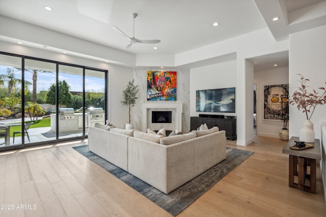 living room featuring light hardwood / wood-style flooring, a premium fireplace, and ceiling fan