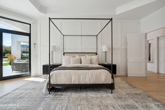 bedroom featuring hardwood / wood-style floors, a tray ceiling, access to outside, and ornamental molding