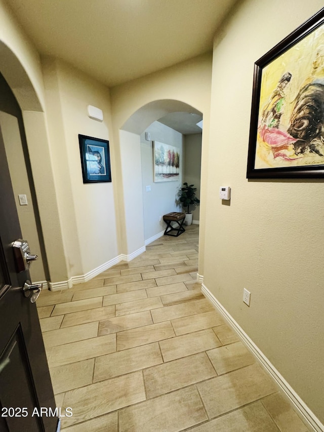 corridor with light wood-style floors, baseboards, and arched walkways