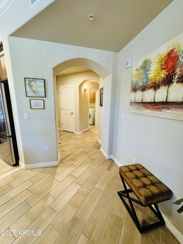hallway with baseboards, light wood-style flooring, washer / clothes dryer, and arched walkways