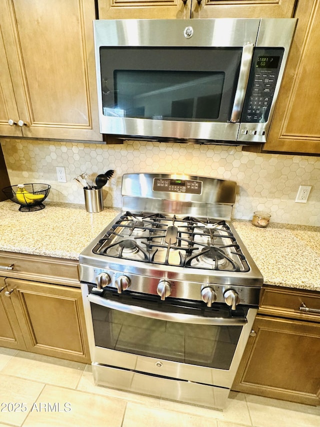 kitchen with light tile patterned floors, stainless steel appliances, light stone counters, and backsplash