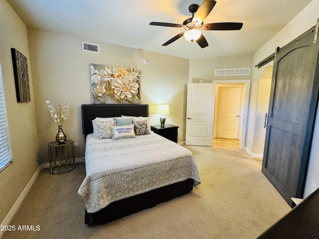 bedroom featuring baseboards, light carpet, a barn door, and visible vents