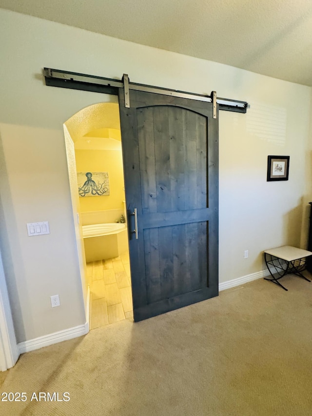 interior space with baseboards, a barn door, carpet floors, and arched walkways