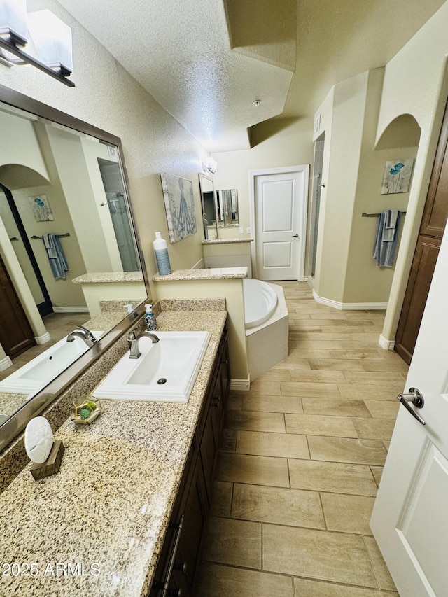 bathroom featuring vanity, wood finish floors, a textured ceiling, and a garden tub
