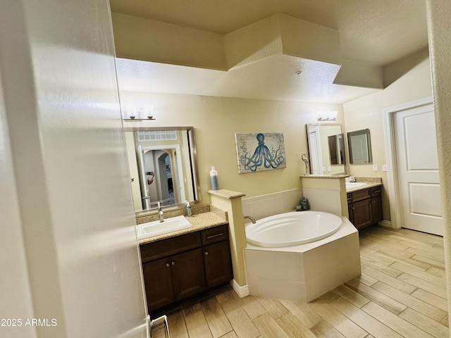bathroom with wood finished floors, a sink, two vanities, a bath, and visible vents