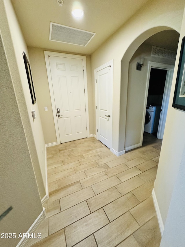 corridor with light wood finished floors, visible vents, baseboards, arched walkways, and washer / dryer