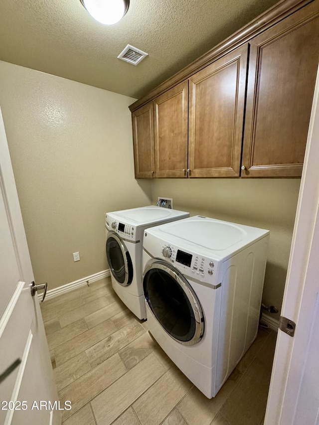 washroom featuring washer and dryer, cabinet space, light wood-type flooring, visible vents, and a textured ceiling