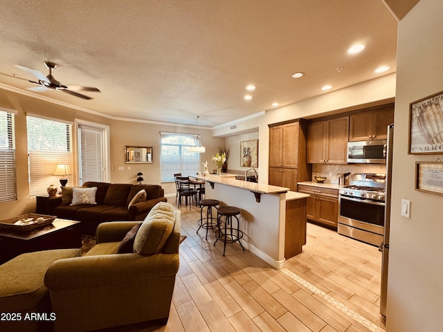 kitchen featuring a kitchen bar, stainless steel appliances, brown cabinetry, open floor plan, and crown molding