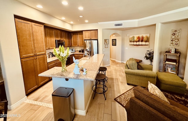 kitchen with light stone countertops, a breakfast bar area, appliances with stainless steel finishes, arched walkways, and light wood-type flooring