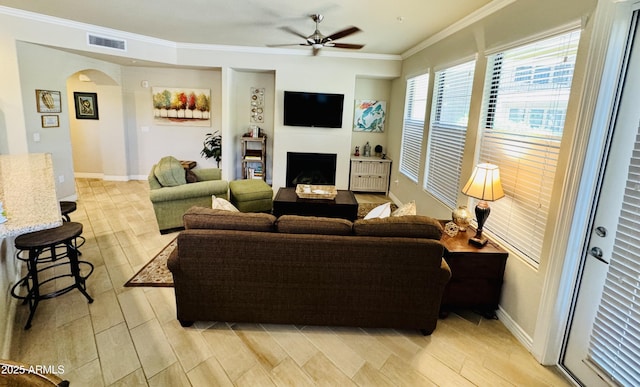 living room featuring ornamental molding, visible vents, a fireplace, arched walkways, and a ceiling fan