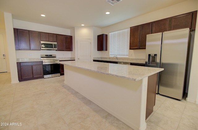 kitchen featuring light tile patterned flooring, dark brown cabinets, a center island, light stone counters, and stainless steel appliances