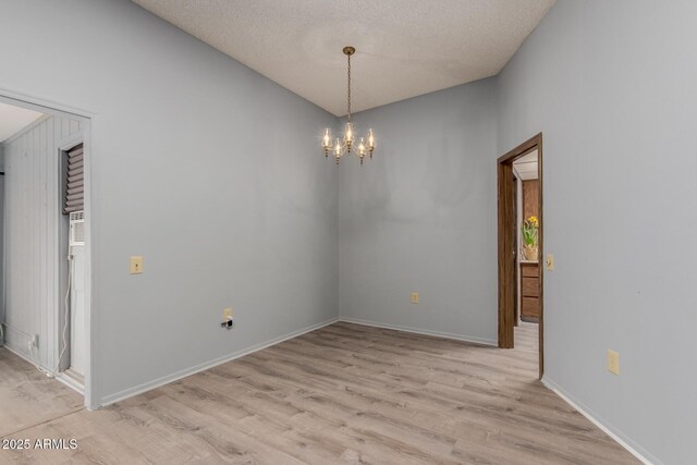 spare room featuring an inviting chandelier, light hardwood / wood-style floors, and a textured ceiling