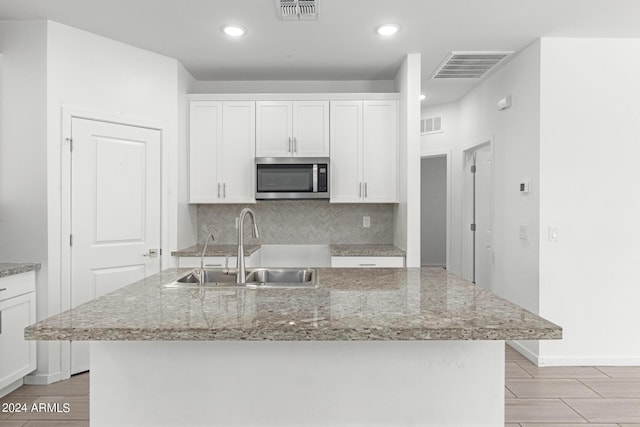 kitchen featuring sink, white cabinetry, a kitchen island with sink, and light stone counters