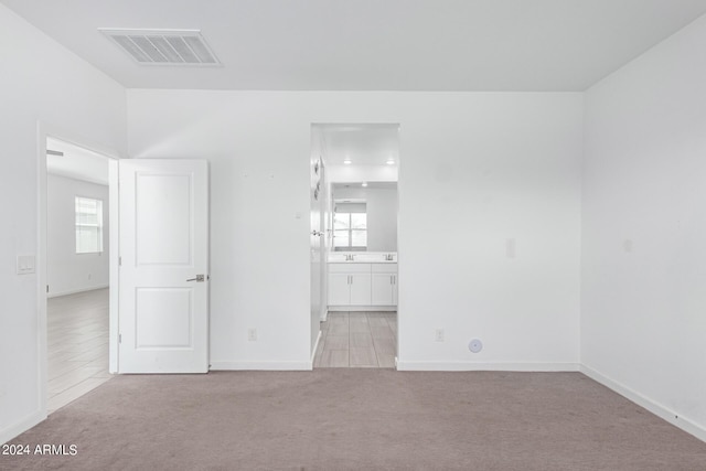 unfurnished bedroom featuring connected bathroom and light carpet