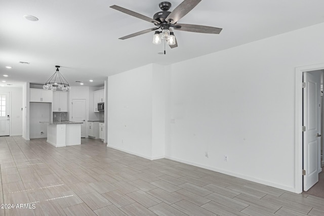 unfurnished living room featuring sink and ceiling fan with notable chandelier