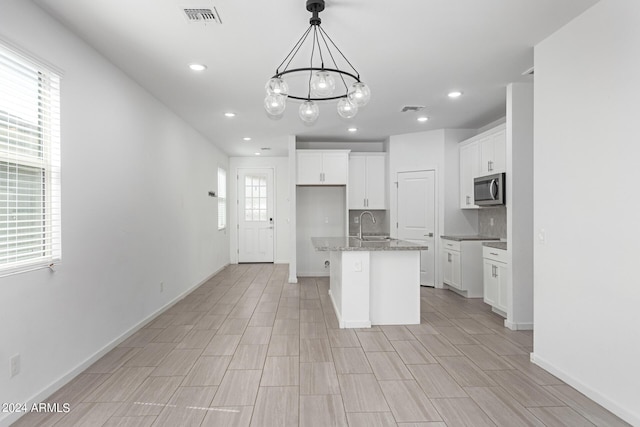 kitchen featuring decorative backsplash, white cabinetry, a chandelier, and an island with sink