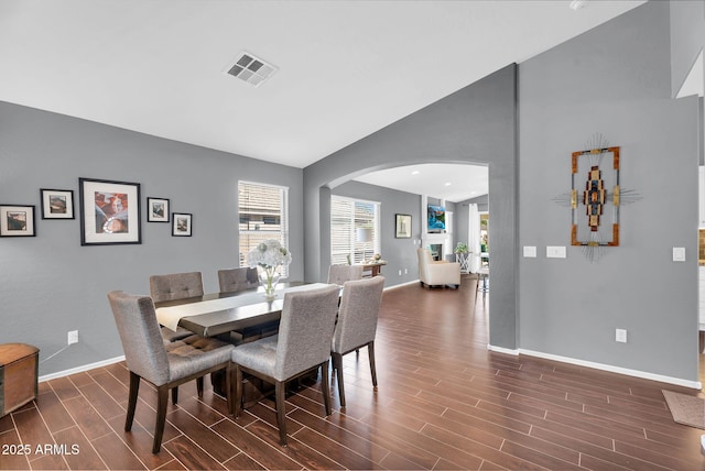 dining area featuring arched walkways, baseboards, dark wood-type flooring, and high vaulted ceiling