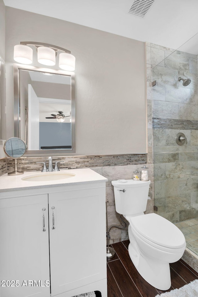 bathroom featuring tiled shower, toilet, vanity, tile walls, and ceiling fan
