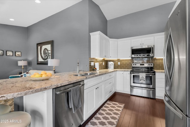 kitchen featuring appliances with stainless steel finishes, a sink, decorative backsplash, light stone countertops, and white cabinetry