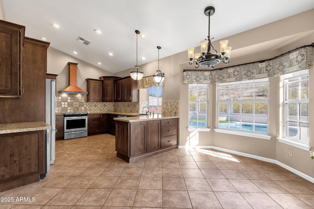 kitchen featuring hanging light fixtures, stainless steel stove, wall chimney exhaust hood, dark brown cabinetry, and light stone countertops