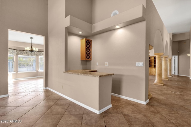 hall featuring decorative columns, dark tile patterned floors, a high ceiling, and a chandelier