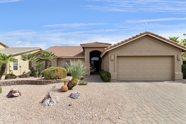 mediterranean / spanish home with an attached garage, a tiled roof, stucco siding, and decorative driveway