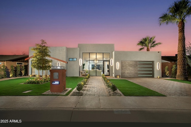 modern home featuring a front lawn, decorative driveway, an attached garage, and stucco siding