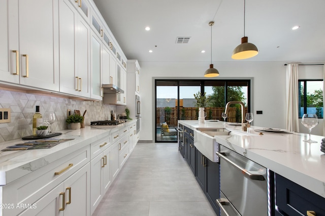 kitchen with light stone counters, stainless steel appliances, visible vents, decorative backsplash, and white cabinets