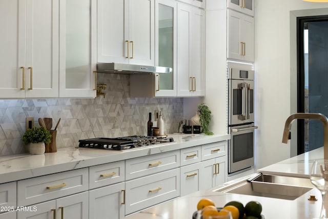 kitchen featuring stainless steel appliances, decorative backsplash, white cabinets, a sink, and under cabinet range hood