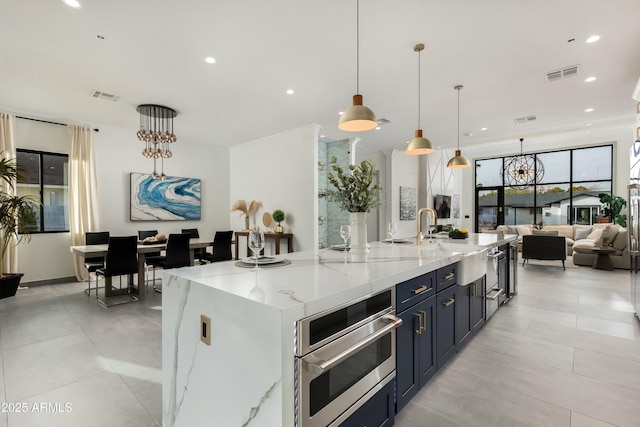 kitchen with light stone countertops, visible vents, a sink, and a large island with sink