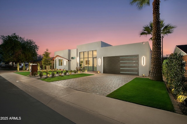 contemporary home with an attached garage, a lawn, decorative driveway, and stucco siding