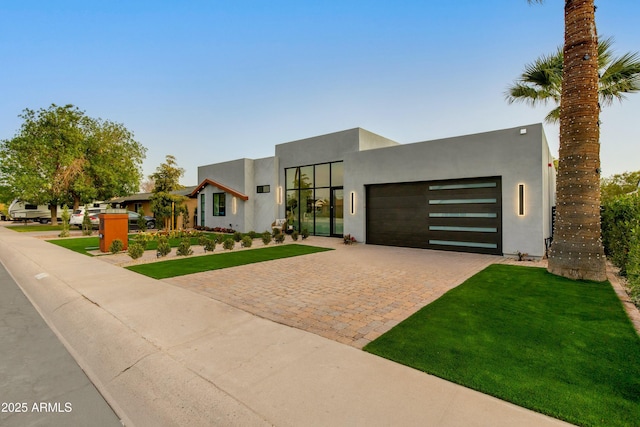 view of front of property with a front yard, decorative driveway, an attached garage, and stucco siding