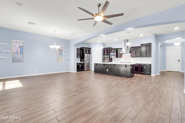 unfurnished living room with light wood finished floors, visible vents, baseboards, ceiling fan with notable chandelier, and arched walkways