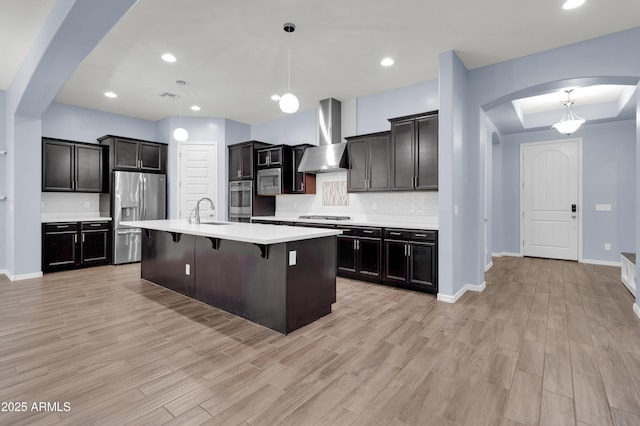 kitchen with wall chimney range hood, light countertops, arched walkways, stainless steel appliances, and a sink